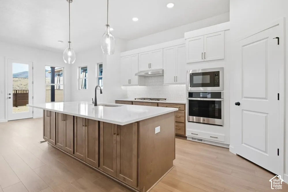 Kitchen featuring a central island with a quartz countertop, wood-finish cabinetry, stainless steel double wall ovens, a tile backsplash, and pendant lighting