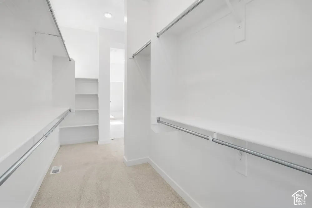 Walk-in storage space featuring built-in shelving, dual-tier metal hanging rods, recessed ceiling lighting, and wall-to-wall carpeting