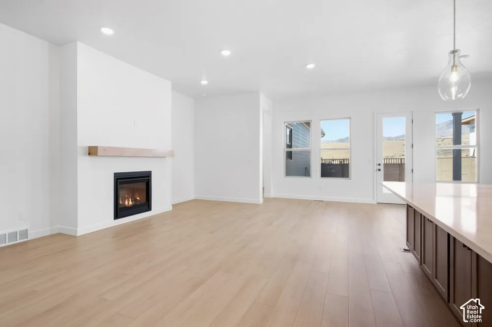 Open-concept interior featuring wood-finish flooring, a fireplace with a natural wood mantel, recessed lighting, and a kitchen island with a neutral countertop