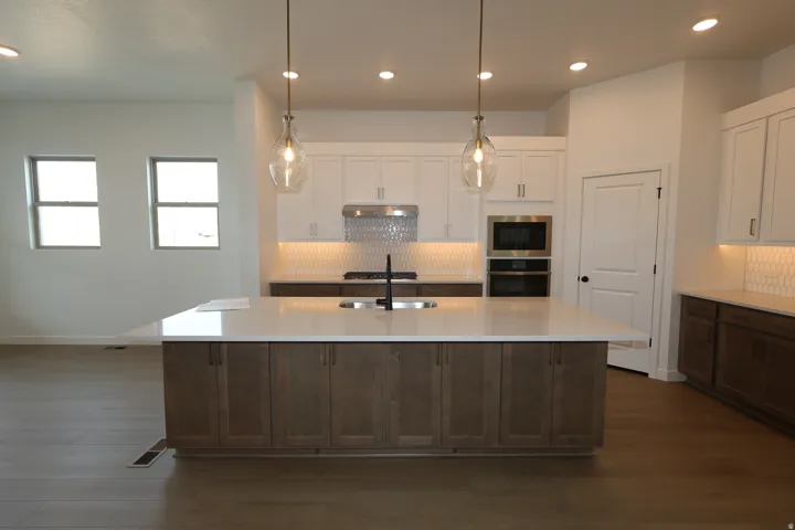 Kitchen featuring a large island with sink, stainless steel appliances, white cabinetry with under-cabinet lighting, and wood-finish flooring