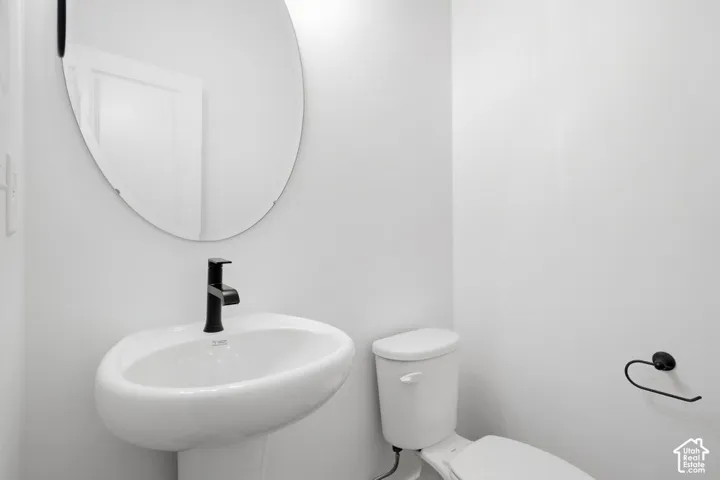 Oval wall-mounted mirror, white pedestal sink, matte black faucet, and matte black hardware