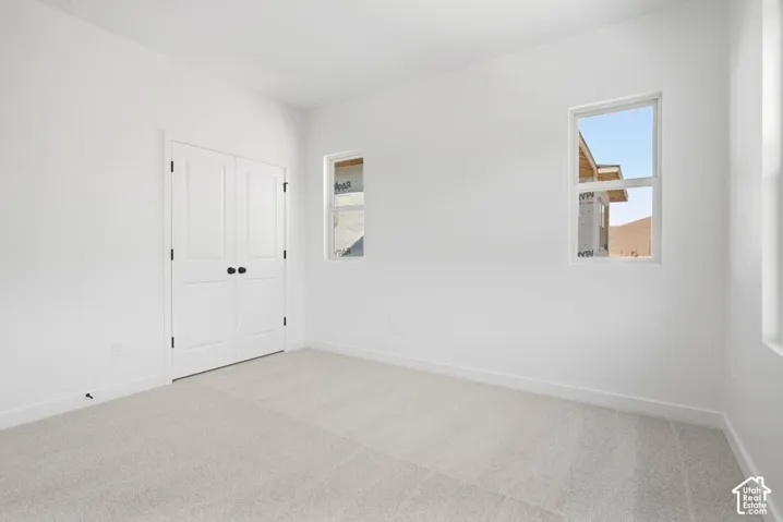 Neutral-toned carpeted flooring, white walls, and double doors featuring matte black hardware, accompanied by two windows