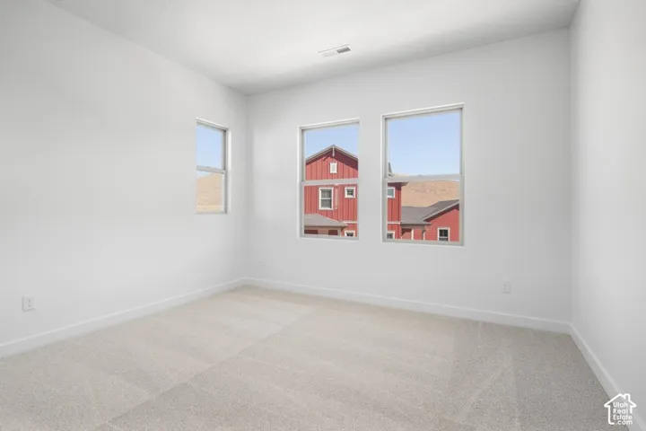 Neutral-toned interior space featuring light-colored wall-to-wall carpeting, crisp white walls, and triple window configuration