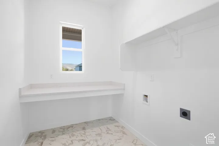 Laundry area featuring light-toned stone-patterned flooring, a built-in countertop, an upper storage shelf, and a window