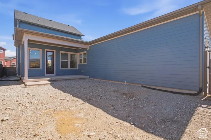Exterior featuring blue horizontal siding, a covered concrete patio, multi-pane windows, and a gravel-surfaced yard