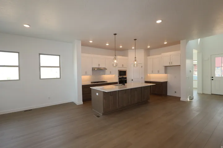 Wood-finish flooring throughout, recessed lighting, kitchen island with seating, stainless steel appliances, and white shaker cabinetry