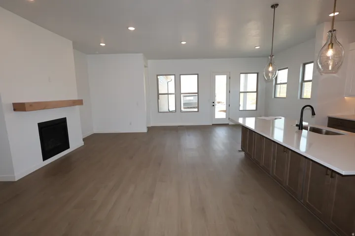 Open-concept living space featuring wood-finish flooring, a built-in fireplace with wood mantel, recessed lighting, and an island with a built-in sink and countertop