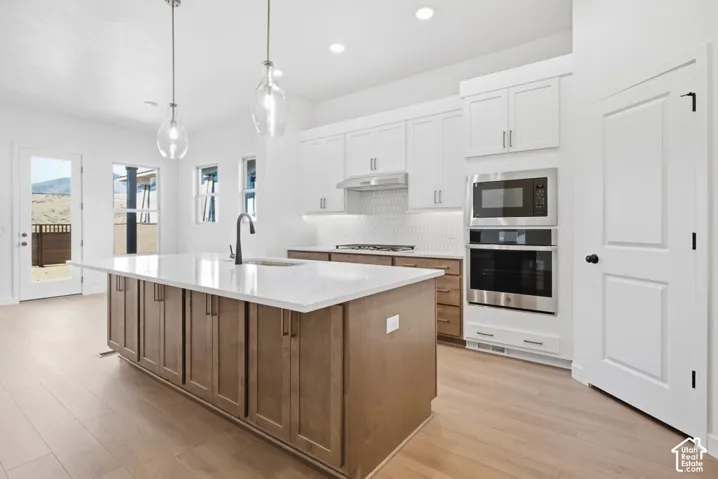 Kitchen featuring a central island with a quartz countertop, wood-finish cabinetry, stainless steel double wall ovens, a tile backsplash, and pendant lighting