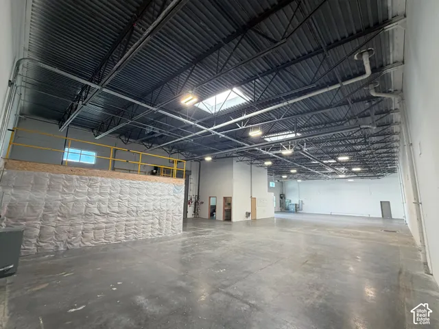 Expansive open-concept industrial space featuring a high ceiling, exposed structural elements, overhead lighting, and a mezzanine level with a safety railing
