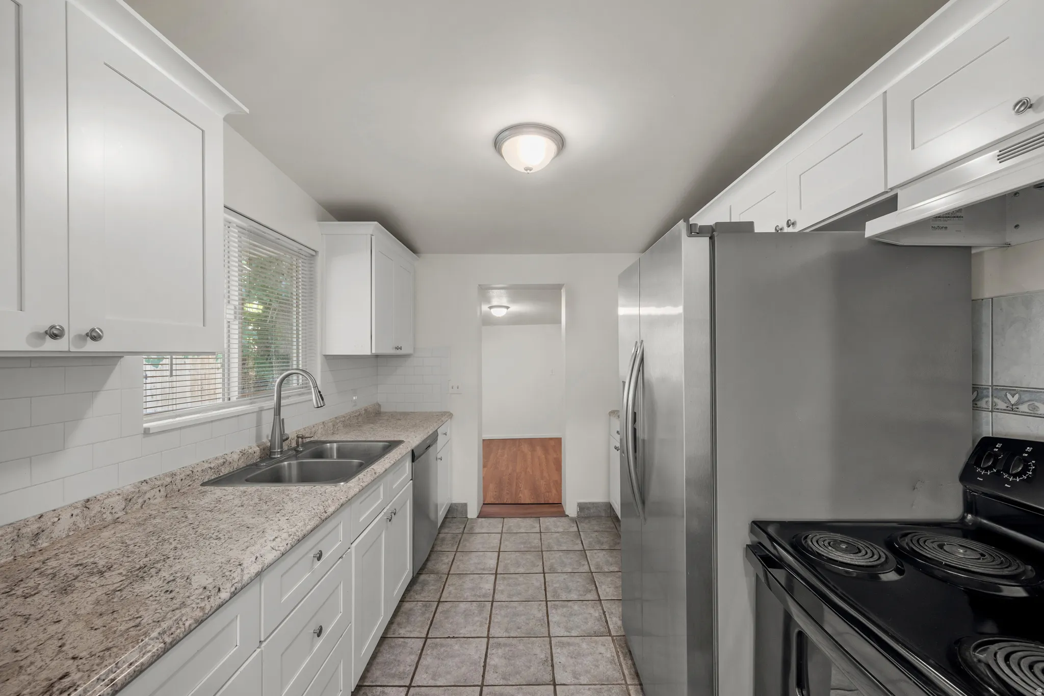 Updated kitchen with white shaker-style cabinetry, expansive countertops, subway tile backsplash, dual basin sink with gooseneck faucet, and stainless steel appliances