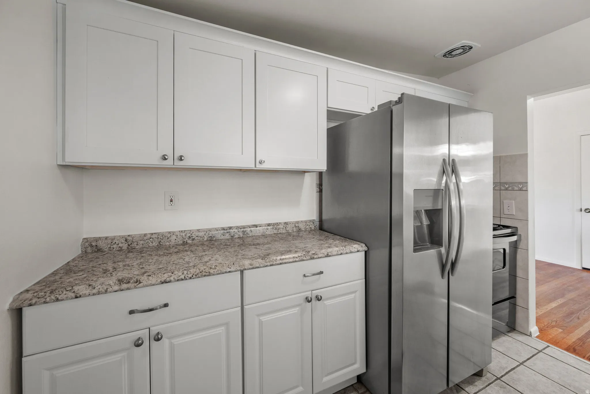 Updated kitchen with white shaker-style cabinetry, expansive countertops, subway tile backsplash, dual basin sink with gooseneck faucet, and stainless steel refrigerator