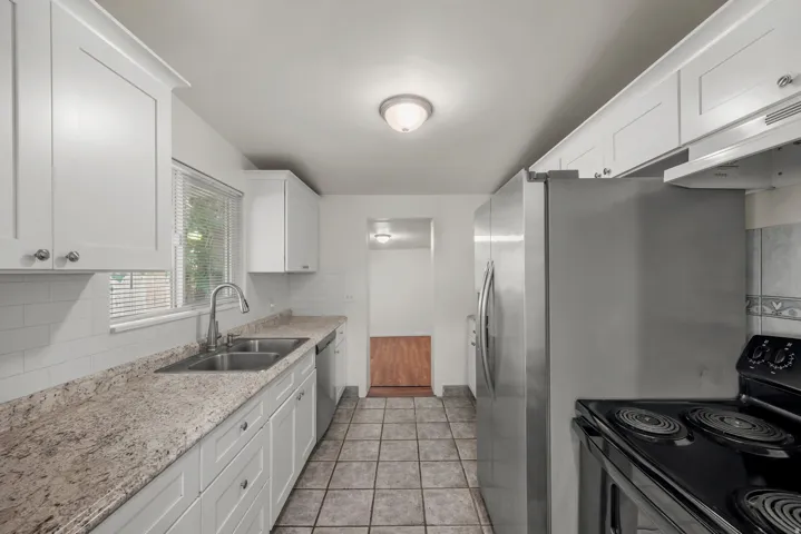 Updated kitchen with white shaker-style cabinetry, expansive countertops, subway tile backsplash, dual basin sink with gooseneck faucet, and stainless steel appliances