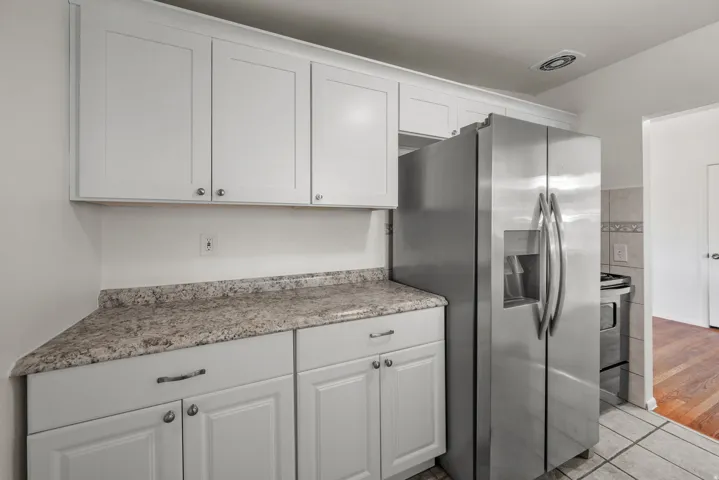 Updated kitchen with white shaker-style cabinetry, expansive countertops, subway tile backsplash, dual basin sink with gooseneck faucet, and stainless steel refrigerator