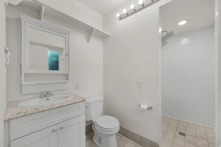 Primary Bathroom featuring a white vanity with a light-toned countertop, a shower with white subway tile, and recessed lighting