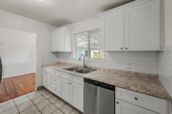 Updated kitchen with white shaker-style cabinetry, expansive countertops, subway tile backsplash, dual basin sink with gooseneck faucet, and stainless steel dishwasher