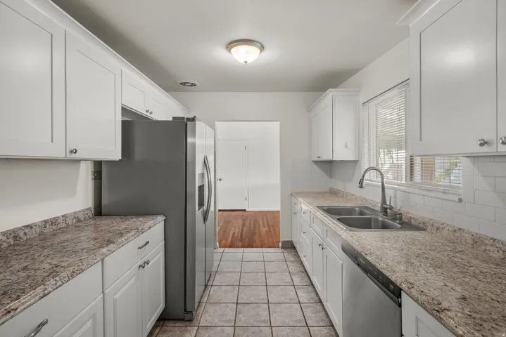 Galley kitchen featuring white cabinetry, light-toned countertops, a subway tile backsplash, and tile flooring