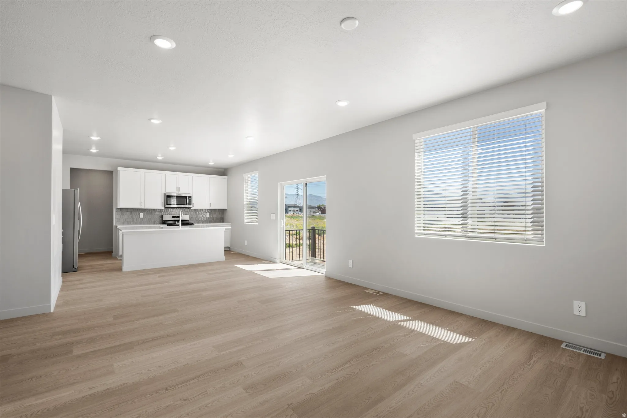Open-concept living area featuring wood-finish flooring, recessed lighting, and a sliding glass door to a balcony