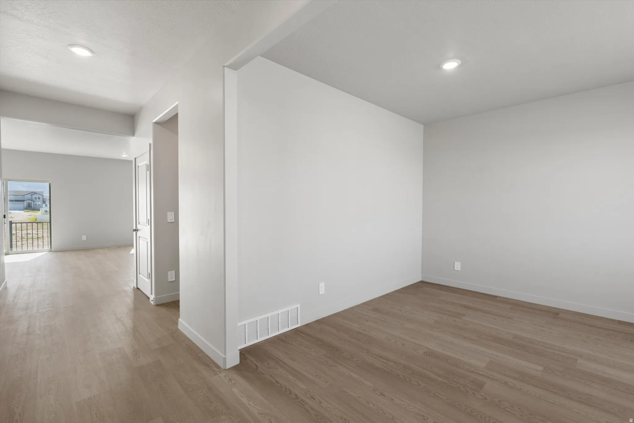 Recessed lighting, wood-finish flooring, white walls, white trim, and a white interior door with dark hardware