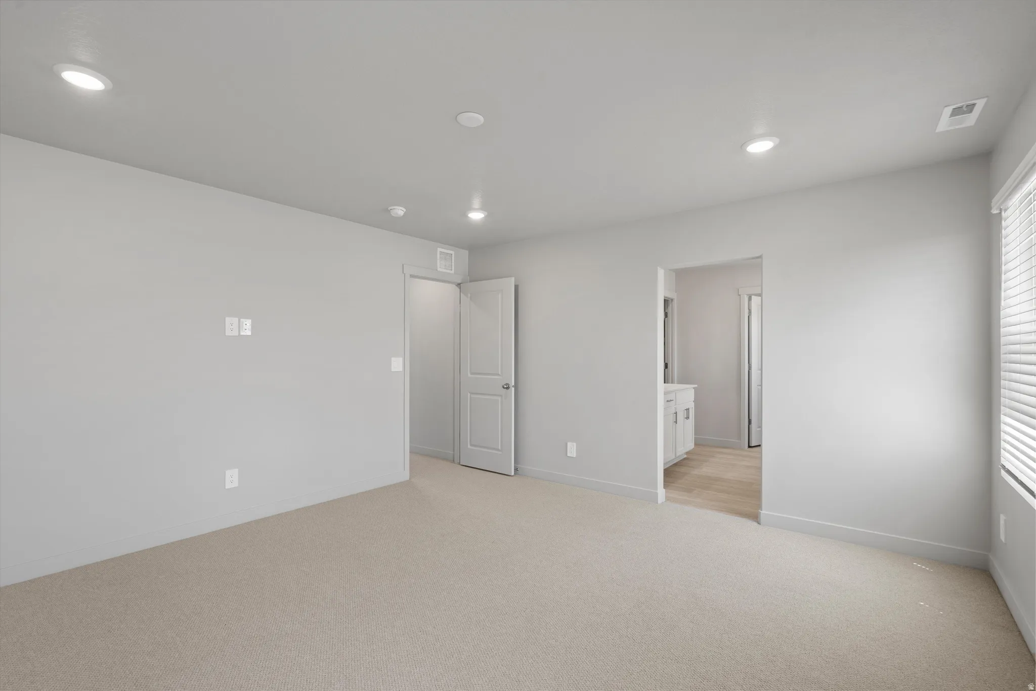 Recessed ceiling lighting, light gray wall paint, light-toned carpet, white window blinds, and white interior doors