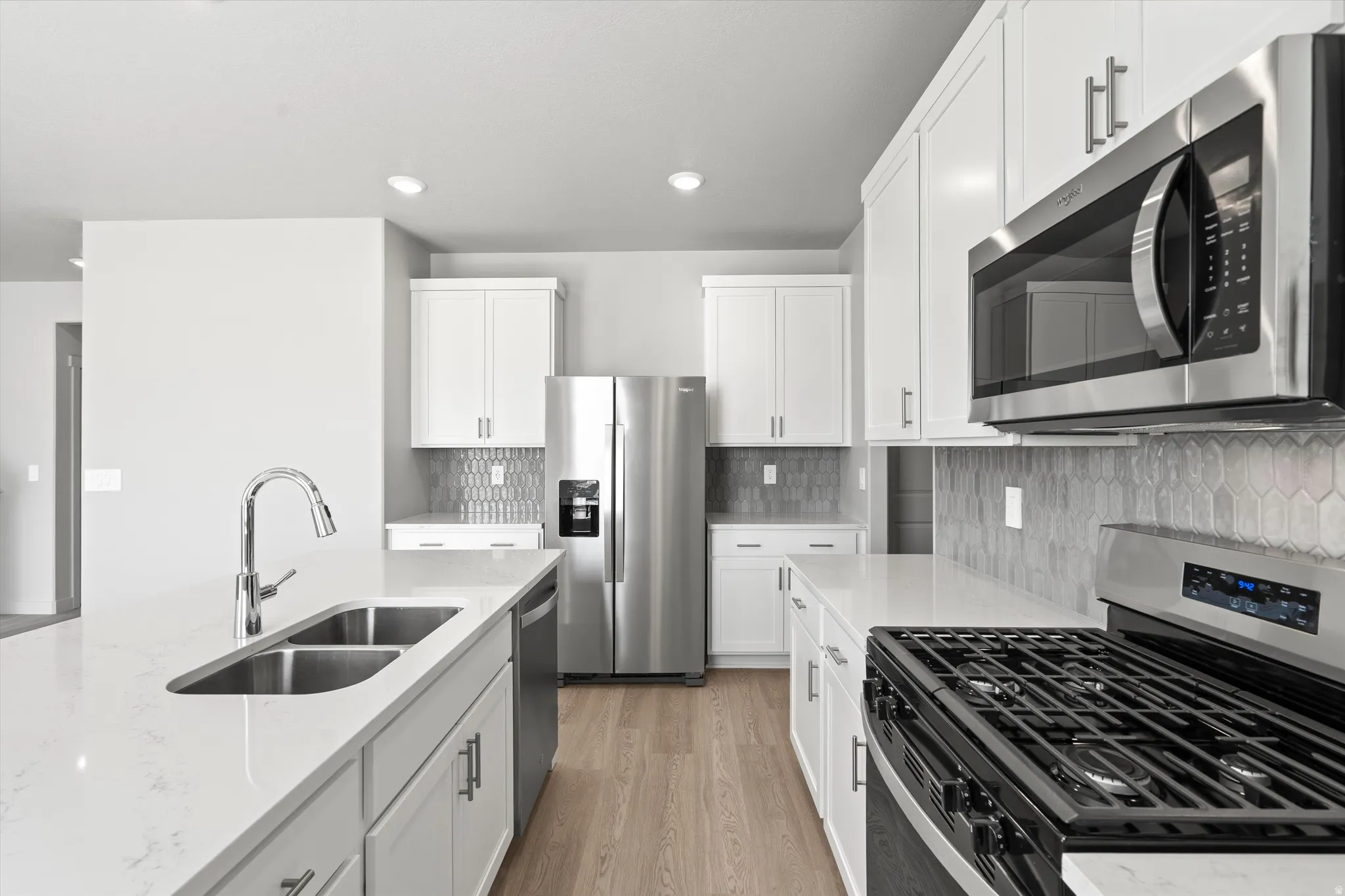 **DISCLIAMER** Some upgrades not photographed. Kitchen with white cabinetry, stainless steel appliances, light-toned wood-finish flooring, and a subway tile backsplash