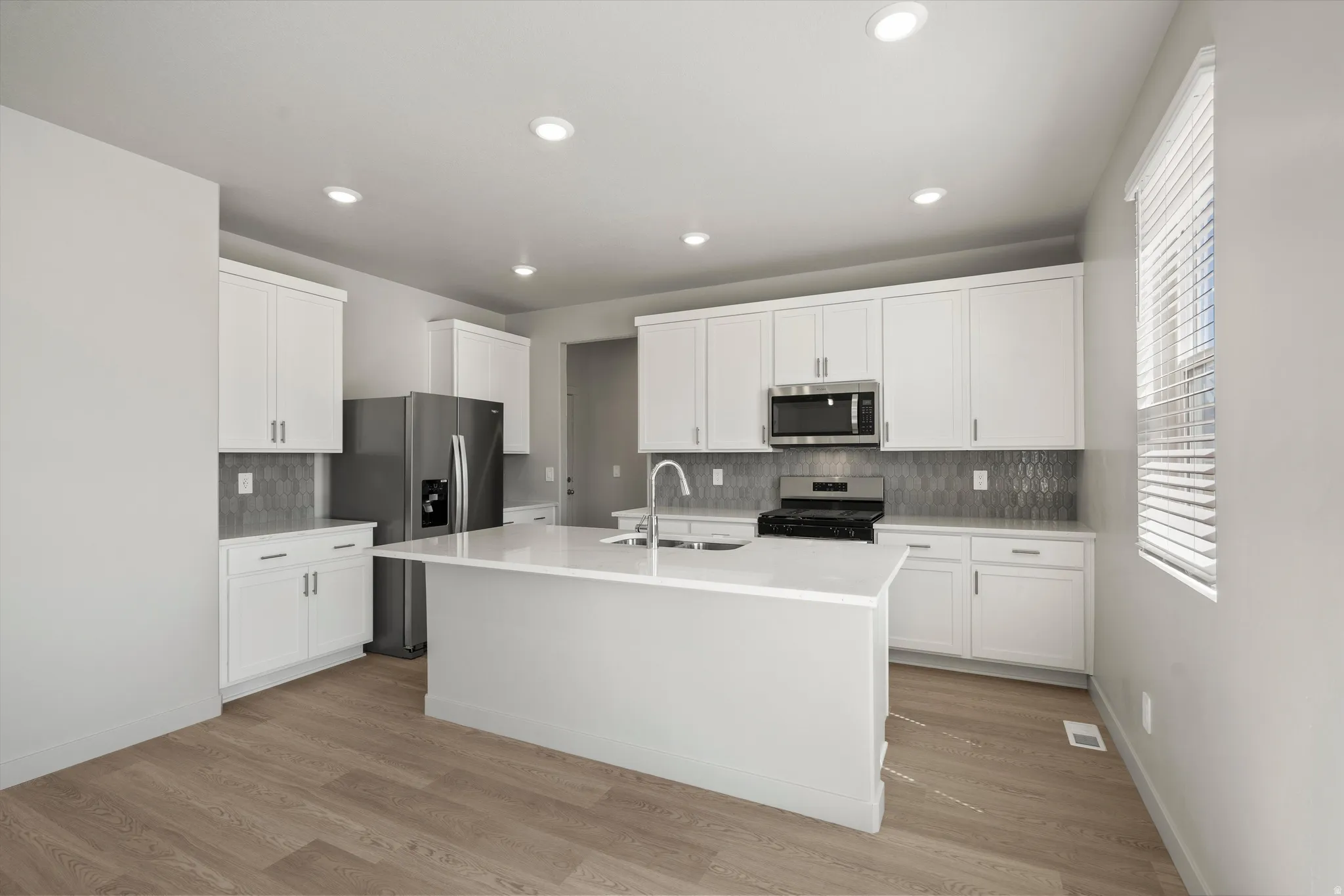 **DISCLIAMER** Some upgrades not photographed. Modern kitchen featuring white cabinetry, a central island, stainless steel appliances, a tiled backsplash, and wood-finish flooring