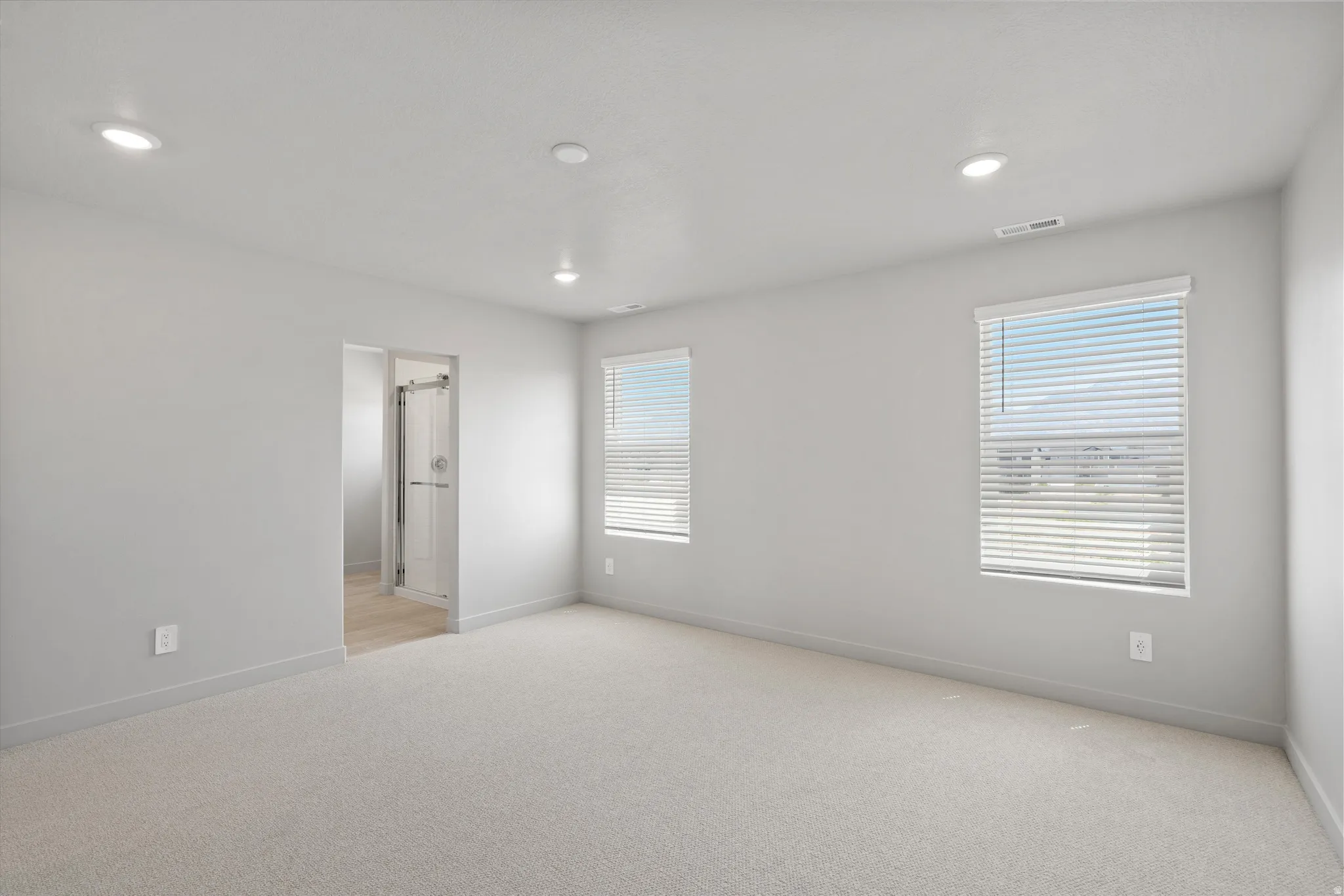 **DISCLIAMER** Some upgrades not photographed. Recessed lighting illuminates this carpeted room, featuring two windows with horizontal blinds and a doorway leading to an enclosed shower