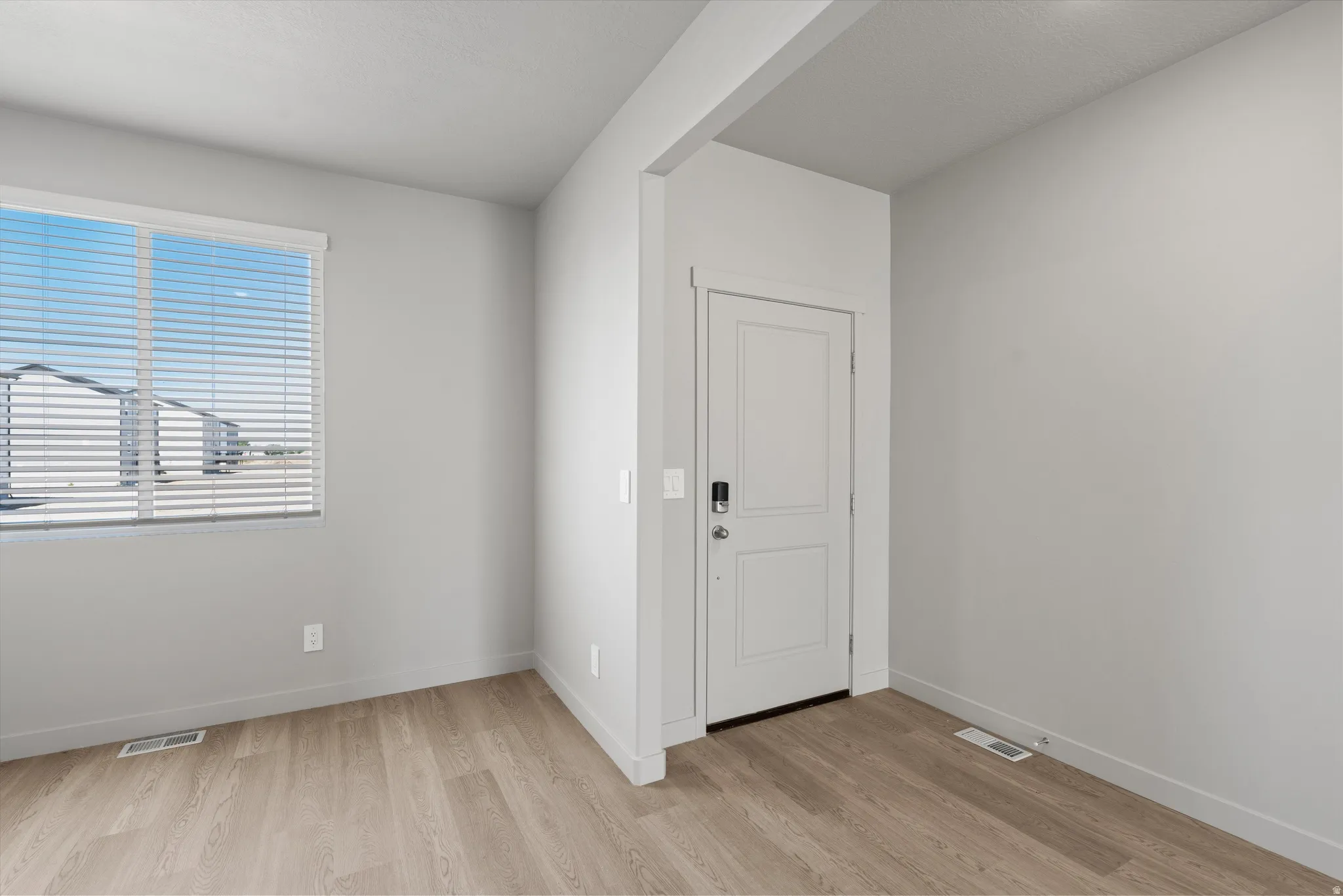Wood-finish flooring, white paneled door, smart lock entry, window with horizontal blinds, neutral wall paint