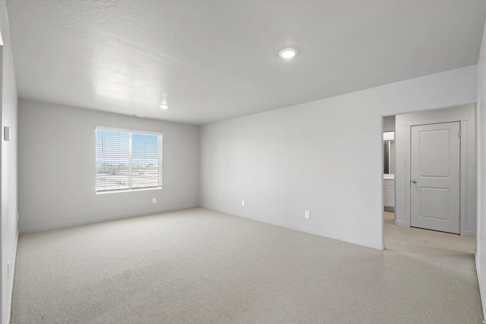 Carpeted room with a window featuring horizontal blinds, recessed lighting, and a neutral color palette