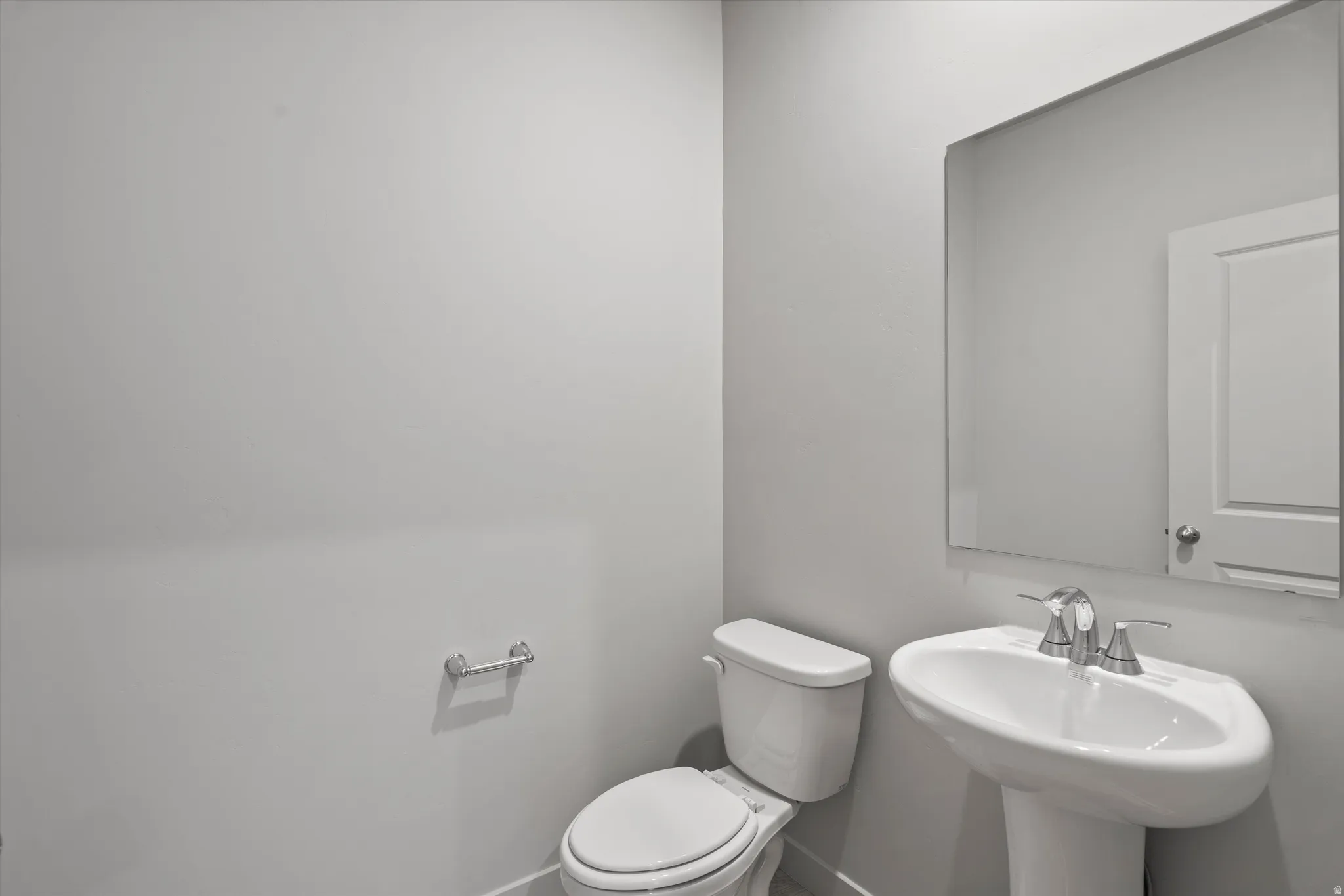 Pedestal sink with chrome-finish faucet, rectangular wall-mounted mirror, and white toilet