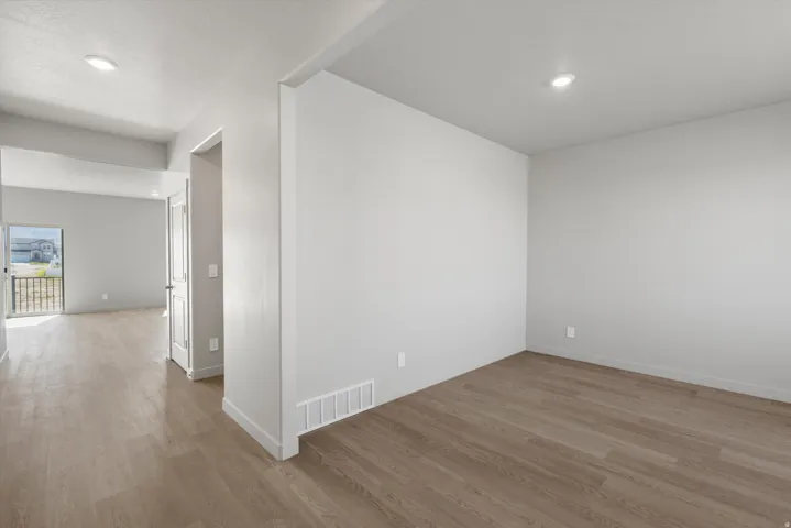 Recessed lighting, wood-finish flooring, white walls, white trim, and a white interior door with dark hardware