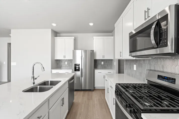 **DISCLIAMER** Some upgrades not photographed. Kitchen with white cabinetry, stainless steel appliances, light-toned wood-finish flooring, and a subway tile backsplash