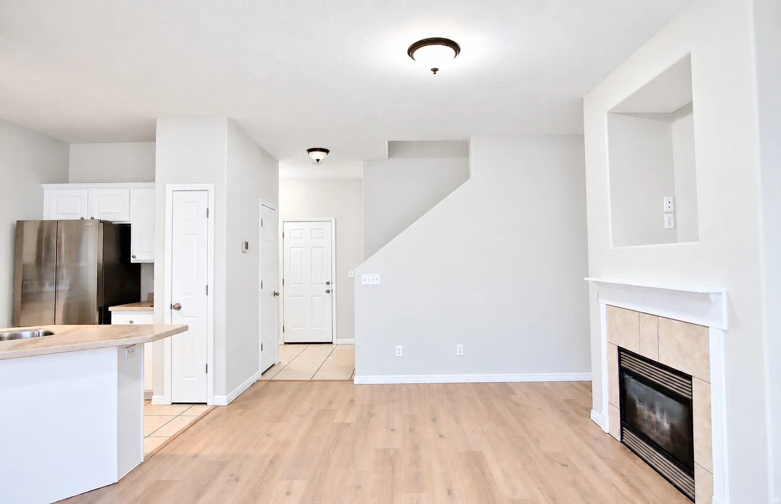Wood-finish flooring, white cabinetry, stainless steel refrigerator, tile-surround fireplace with mantel, and recessed wall niche