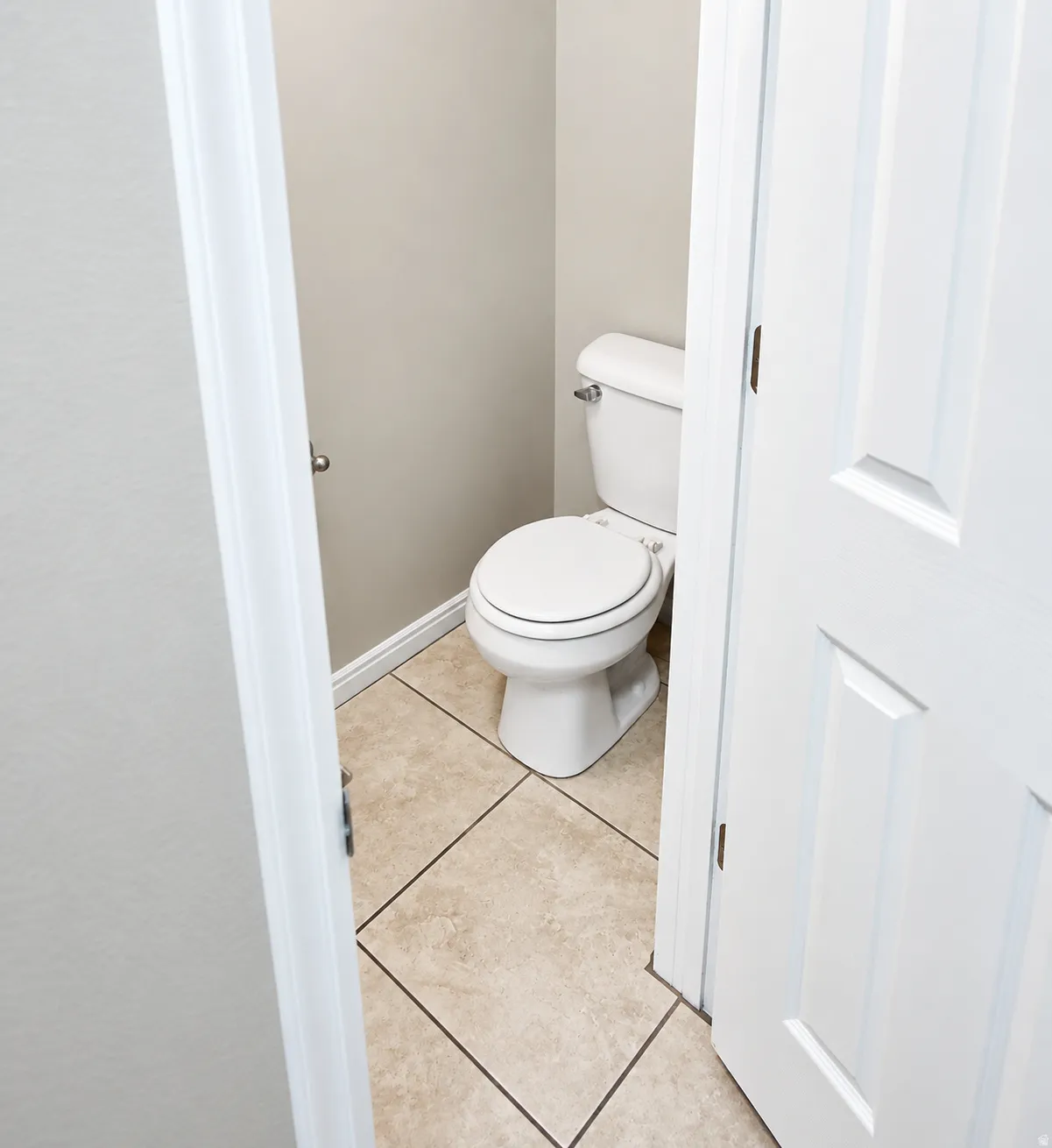 White toilet with a round bowl, neutral wall paint, and light-toned tile flooring