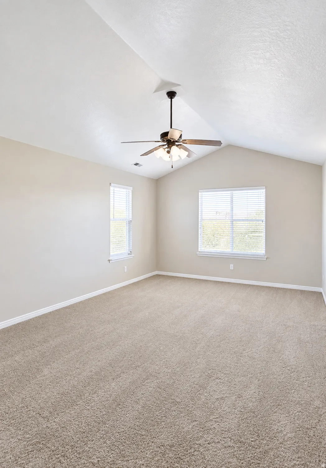 Vaulted ceiling with a ceiling fan, dual windows with blinds, and neutral carpeting