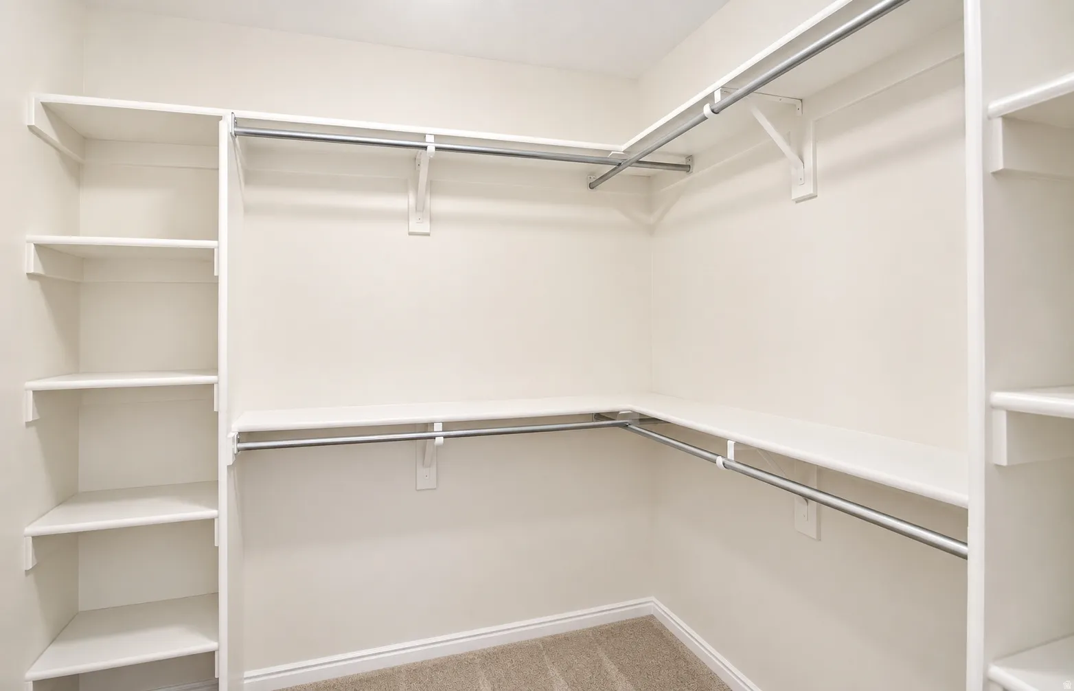 Primary closet with built-in shelving, multiple hanging rods, and neutral carpet flooring