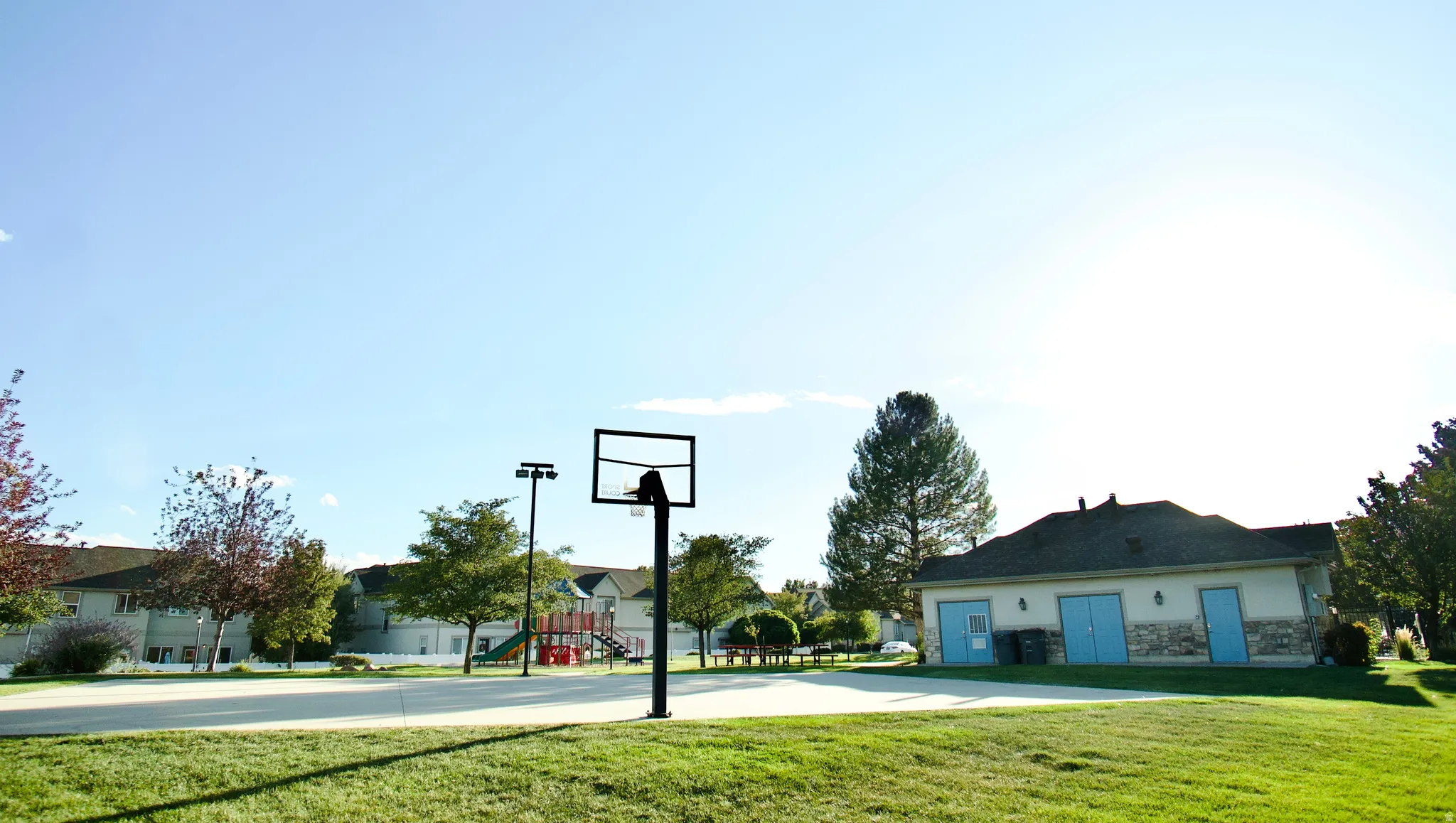 Basketball court with surrounding green space, adjacent to a recreation building  and an outdoor play structure