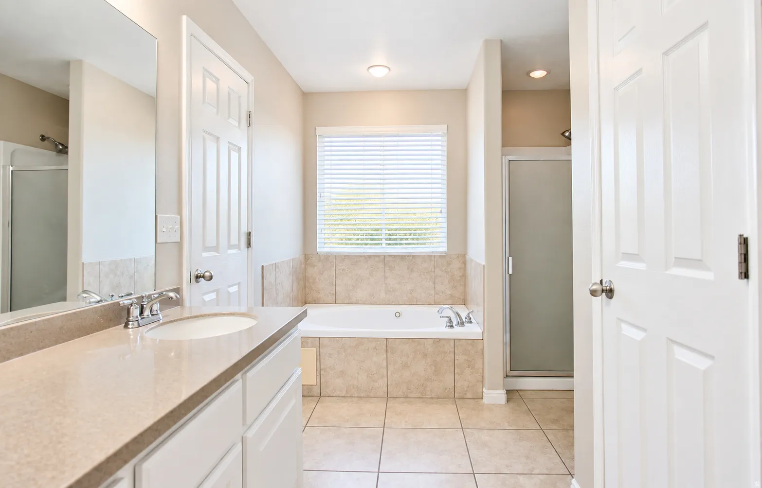 En-suite primary bath with built-in vanity with a single sink, an integrated bathtub with tiled surround, a separate glass-enclosed shower, and tiled flooring