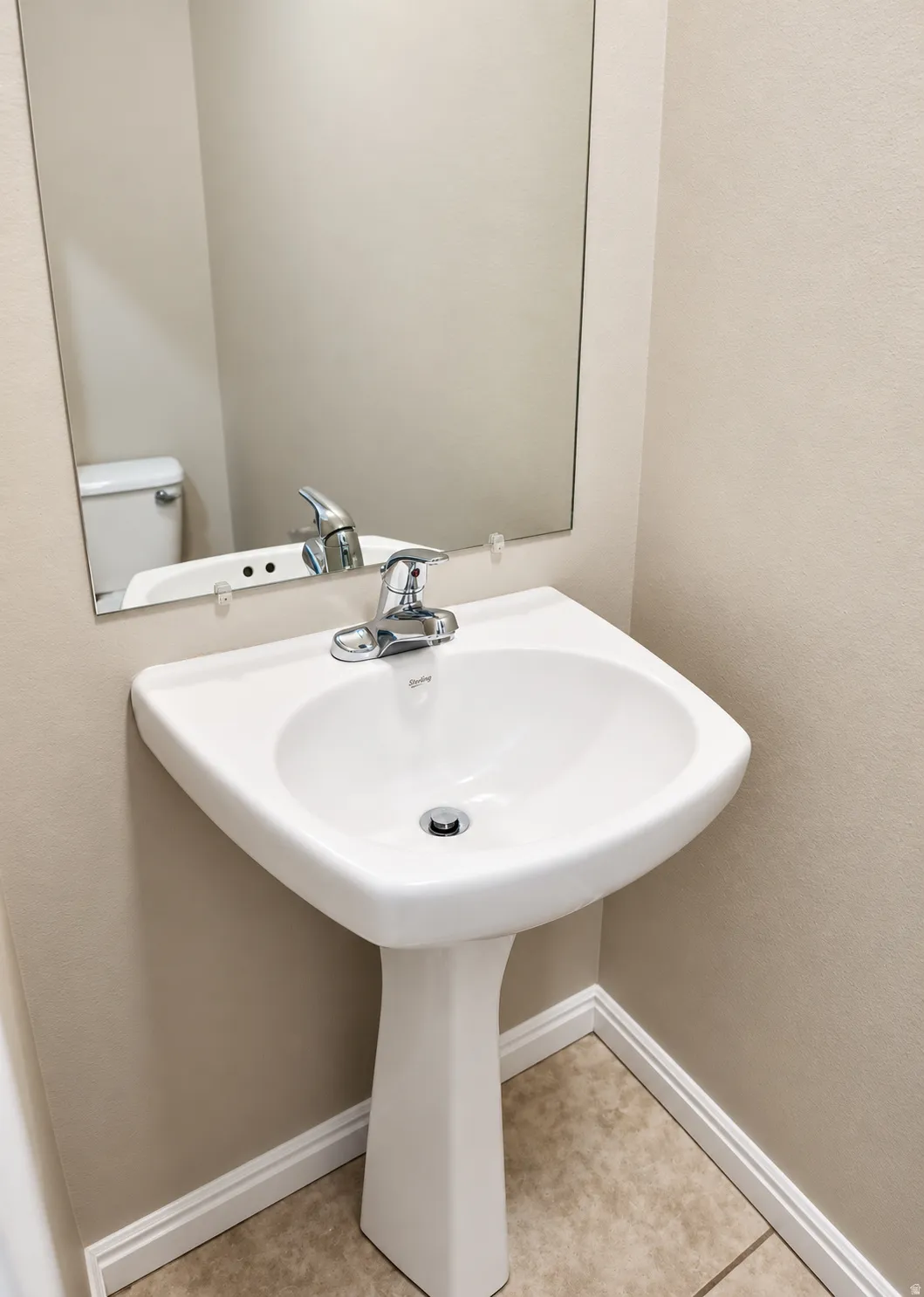 Pedestal sink with chrome faucet, wall-mounted mirror, and tile flooring