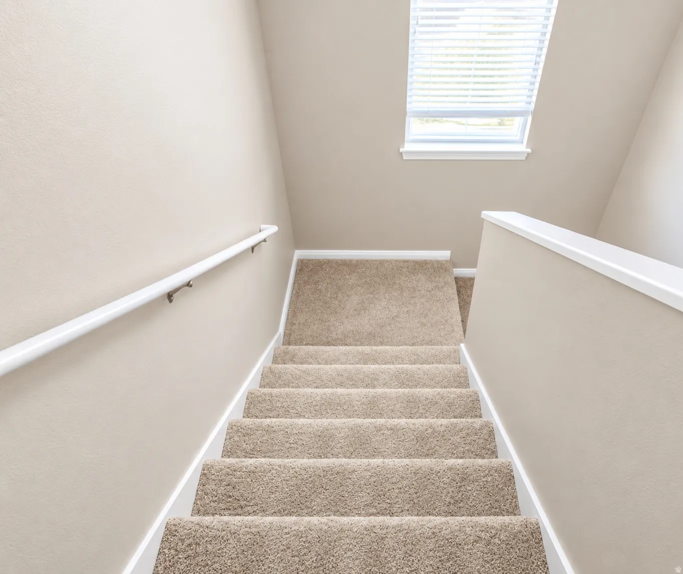 Carpeted staircase with a window featuring blinds and a white handrail