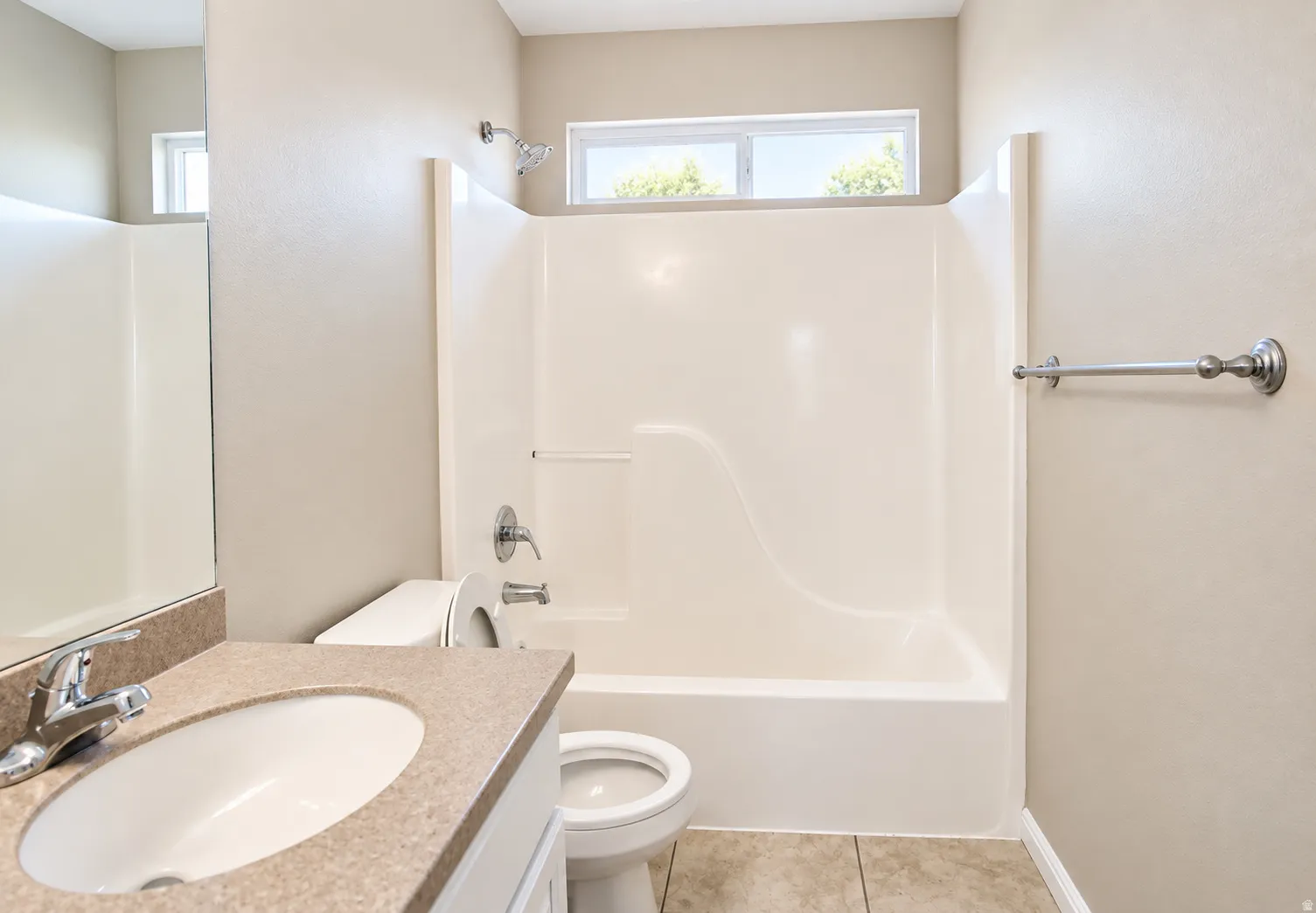 White tub and shower combination with chrome fixtures, a toilet, a vanity with an integrated sink and countertop, and a window for natural light