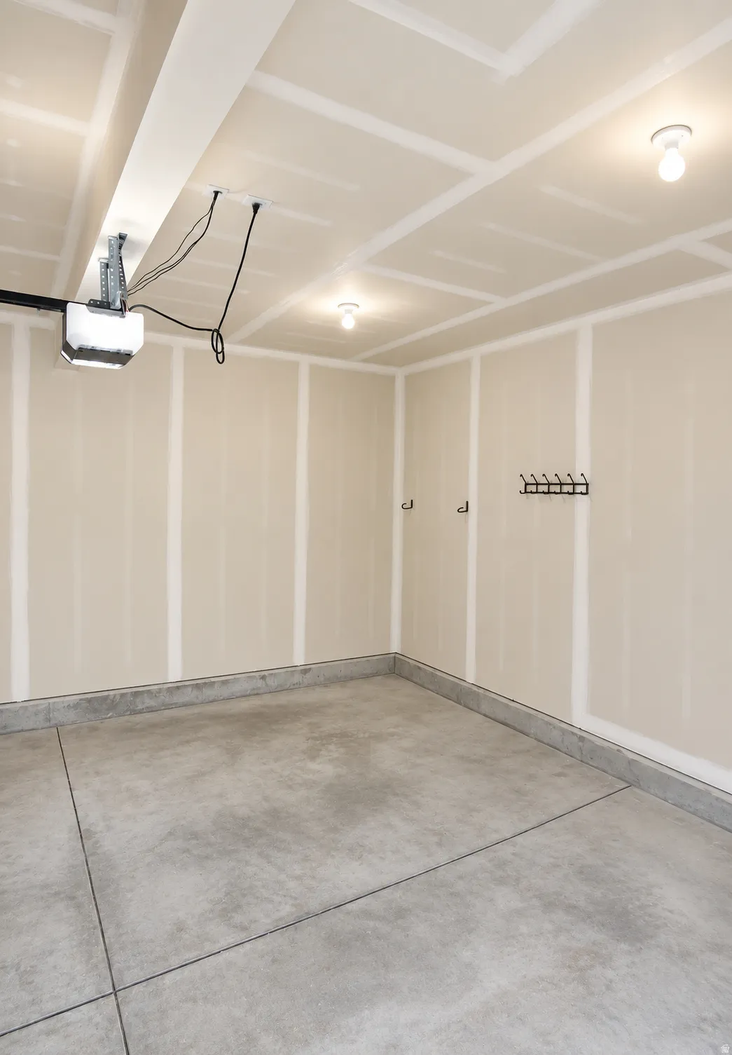Concrete flooring, finished drywall walls, overhead lighting, and an installed garage door opener