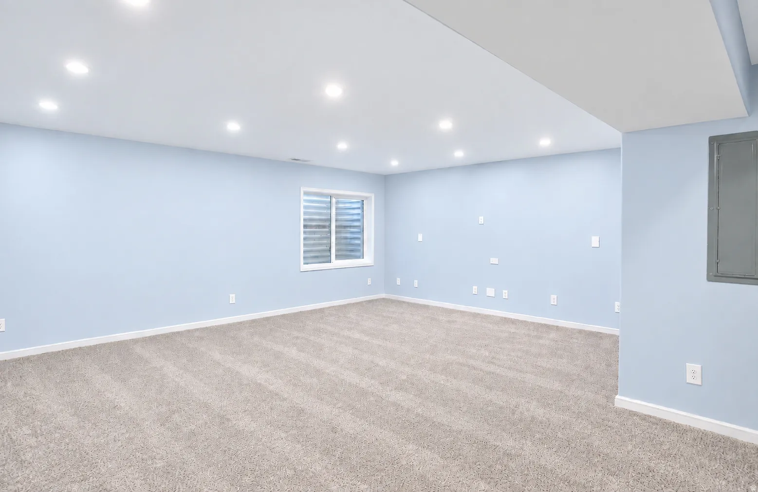 Recessed lighting, light blue wall paint, window with blinds, light-toned carpet, white trim