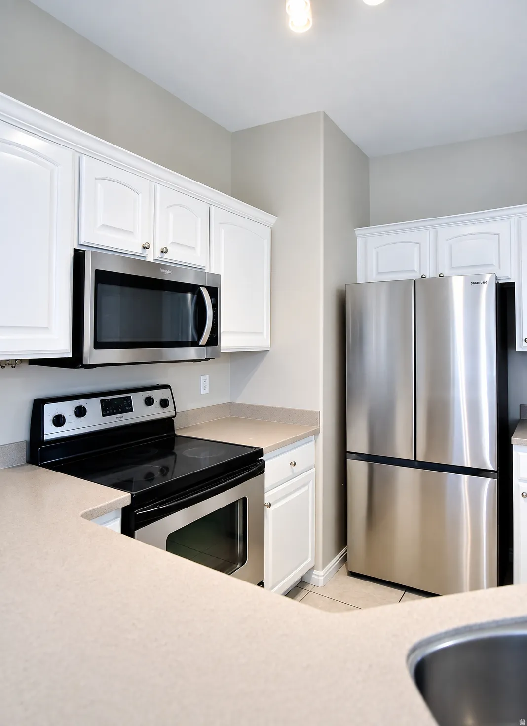 Kitchen featuring white cabinetry, light-toned countertops, stainless steel appliances, and tile flooring