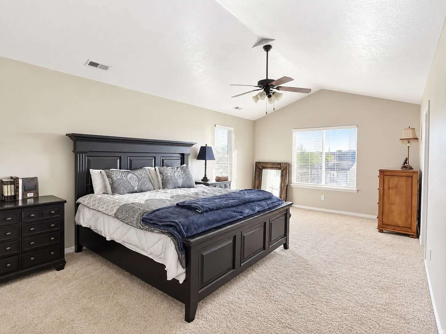 Vaulted ceiling with a ceiling fan, dual windows with blinds, and neutral carpet flooring