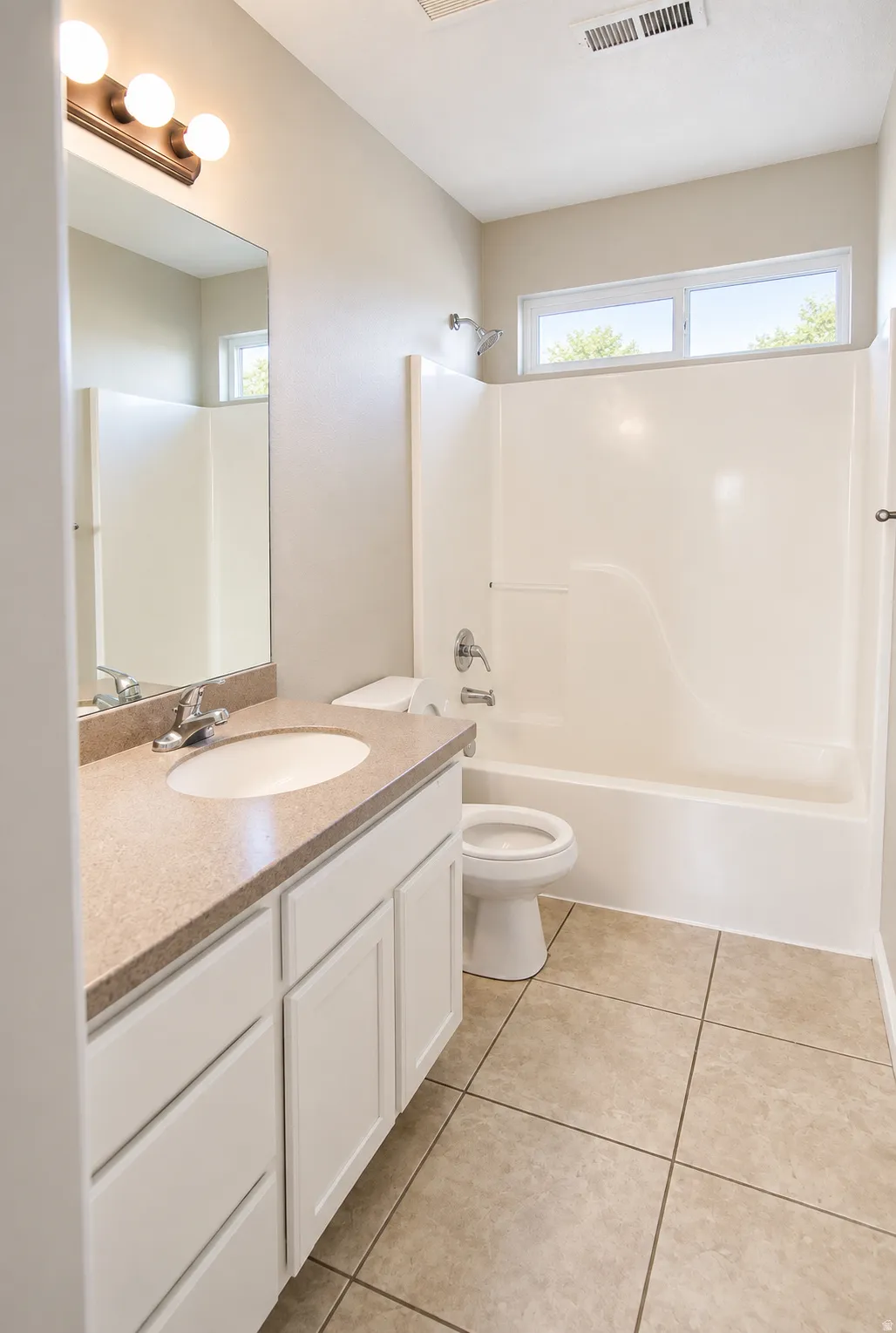 Guest bathroom with full vanity with integrated sink and stone-finish countertop, tiled flooring, white bathtub with shower, and transom windows
