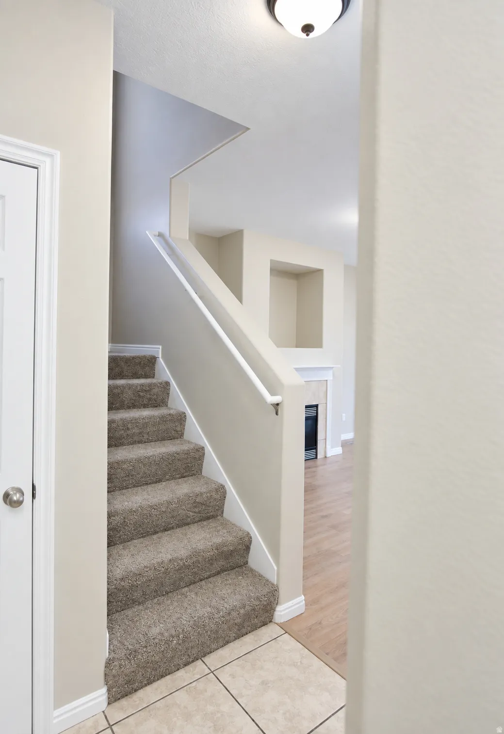 Carpeted staircase with white railing, tile flooring, and a flush mount light fixture