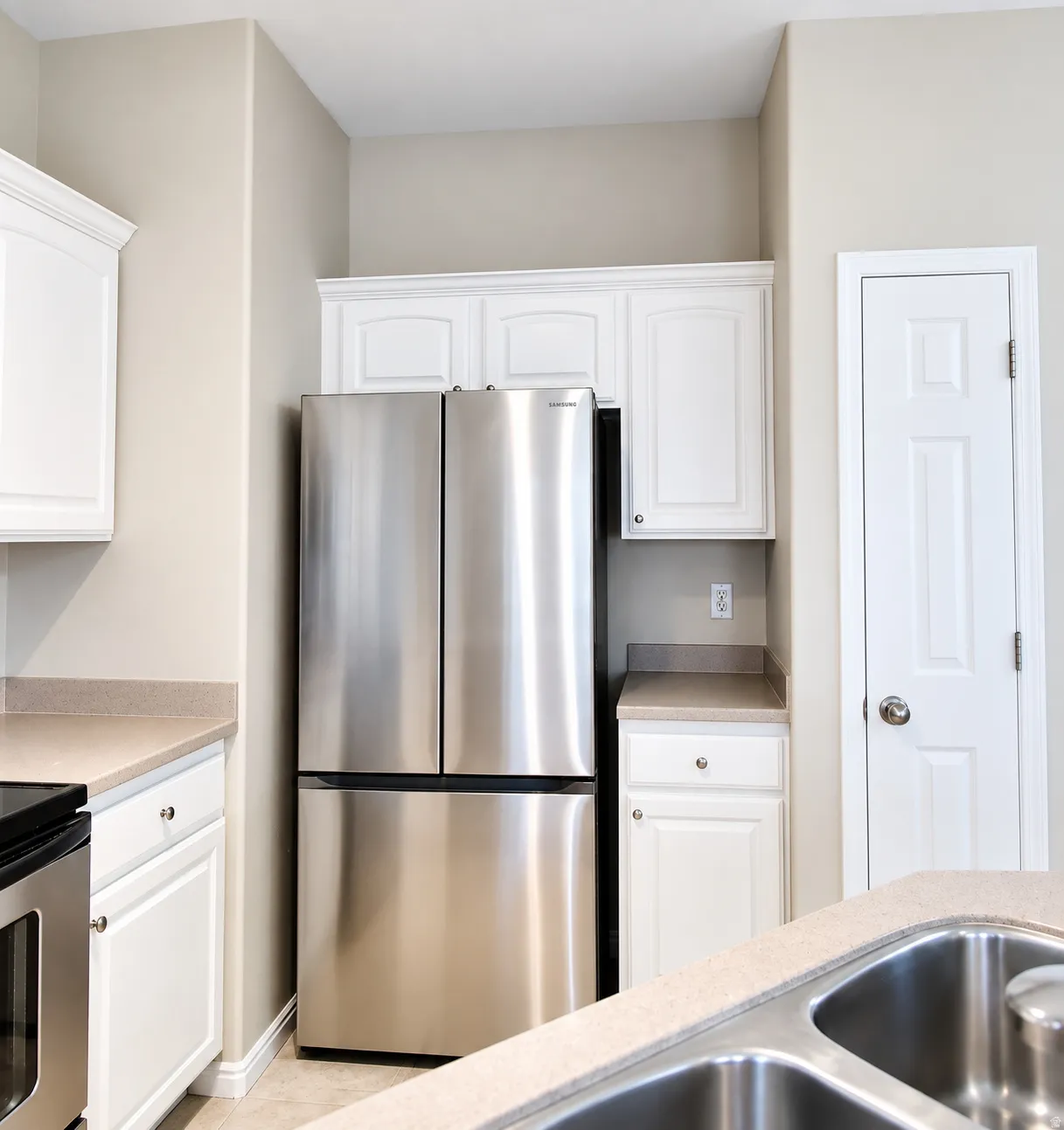 Stainless steel French door refrigerator, white upper and lower cabinetry, light-toned countertops, and a double basin stainless steel sink