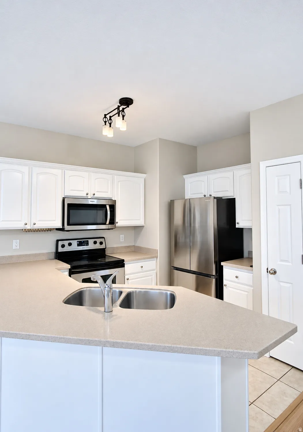 Kitchen featuring an island with a dual basin sink, white cabinetry, stainless steel appliances, and light-toned countertops