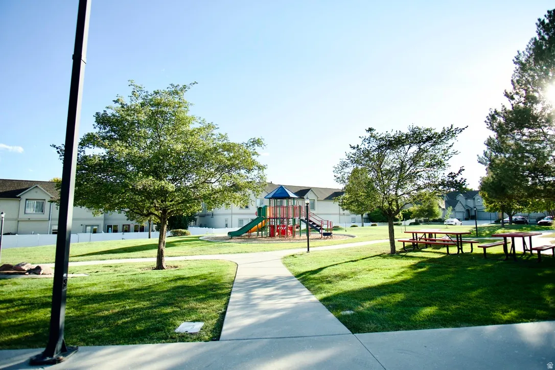 Community green space featuring a playground, multiple picnic tables, mature trees, and paved pathways