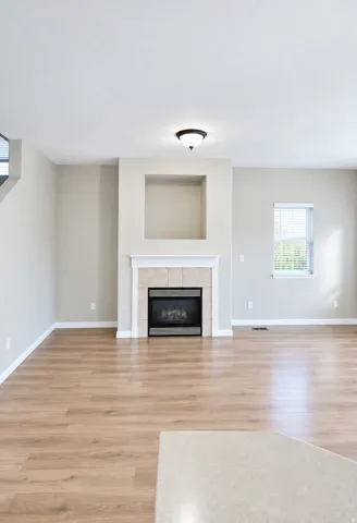 Fireplace with tile surround and mantel, wood-finish flooring, recessed wall niche, window with blinds, and ceiling-mounted light fixture